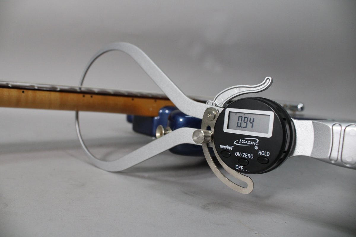 A digital caliper measures the guitar's neck, showing "0.94" on its screen, with the blue body visible behind it.