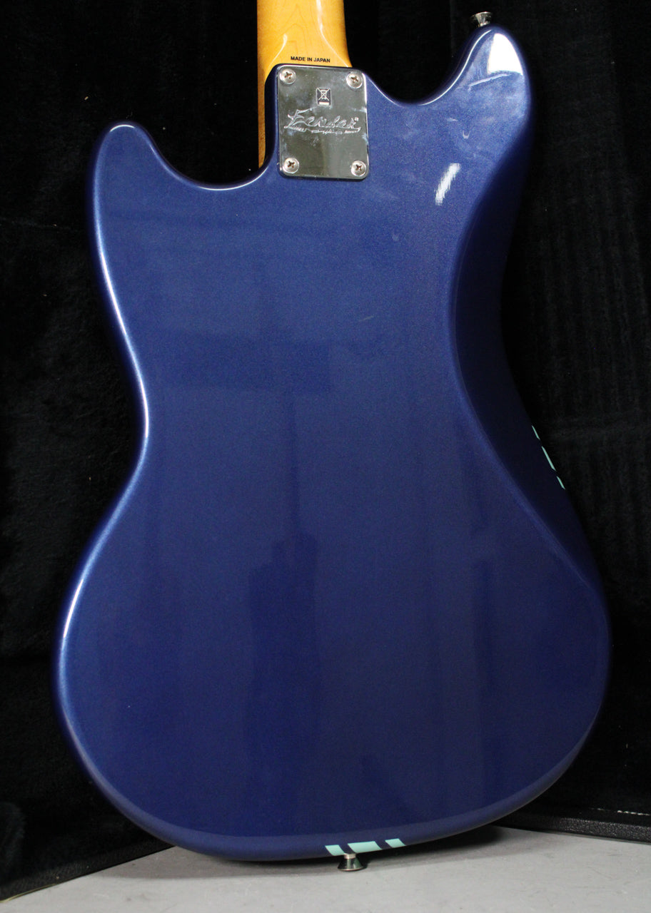 The back of a metallic blue guitar body, with a light racing stripe near the bottom and a chrome neck plate.