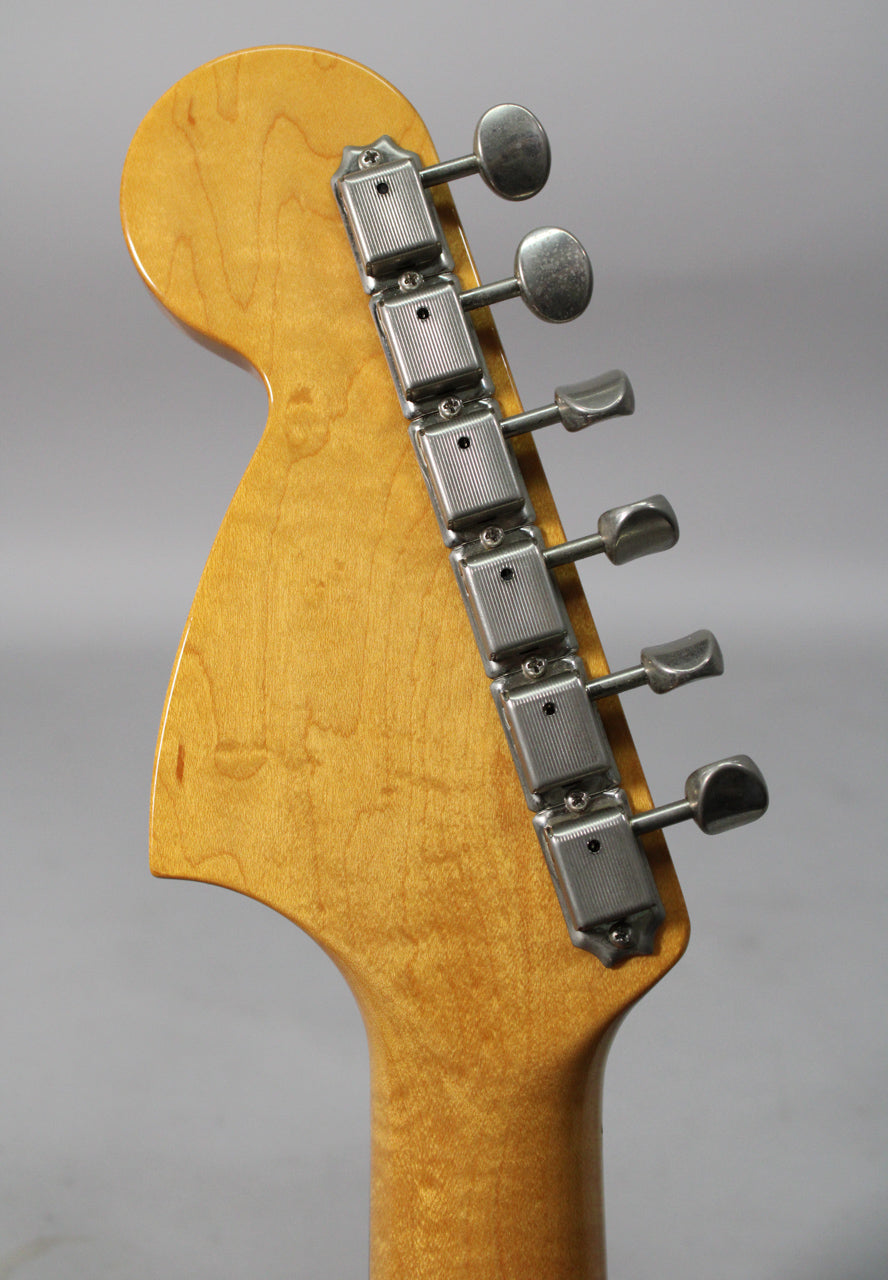 The back of a light brown, glossy headstock with six chrome tuners, showing some light wear and minor scratches.