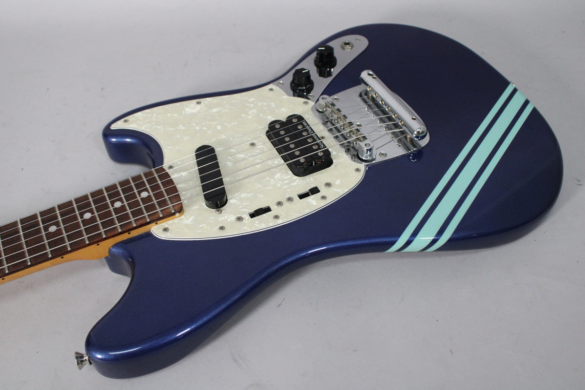 The blue metallic guitar body, with two light blue racing stripes, is angled from the neck to the lower bout, showing the pearloid pickguard.