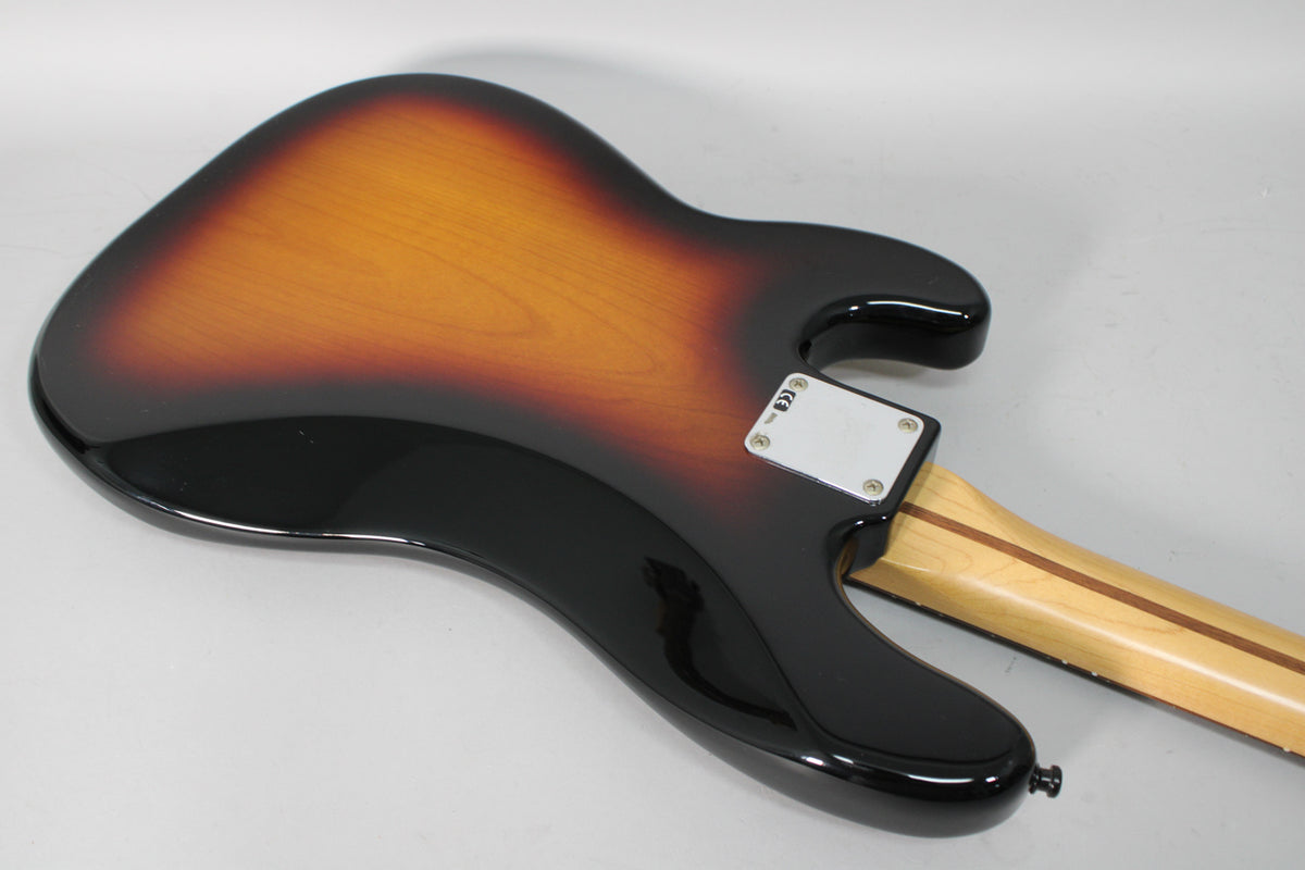 The bass's glossy sunburst body and neck plate are viewed from the back, with the light-colored neck extending right.