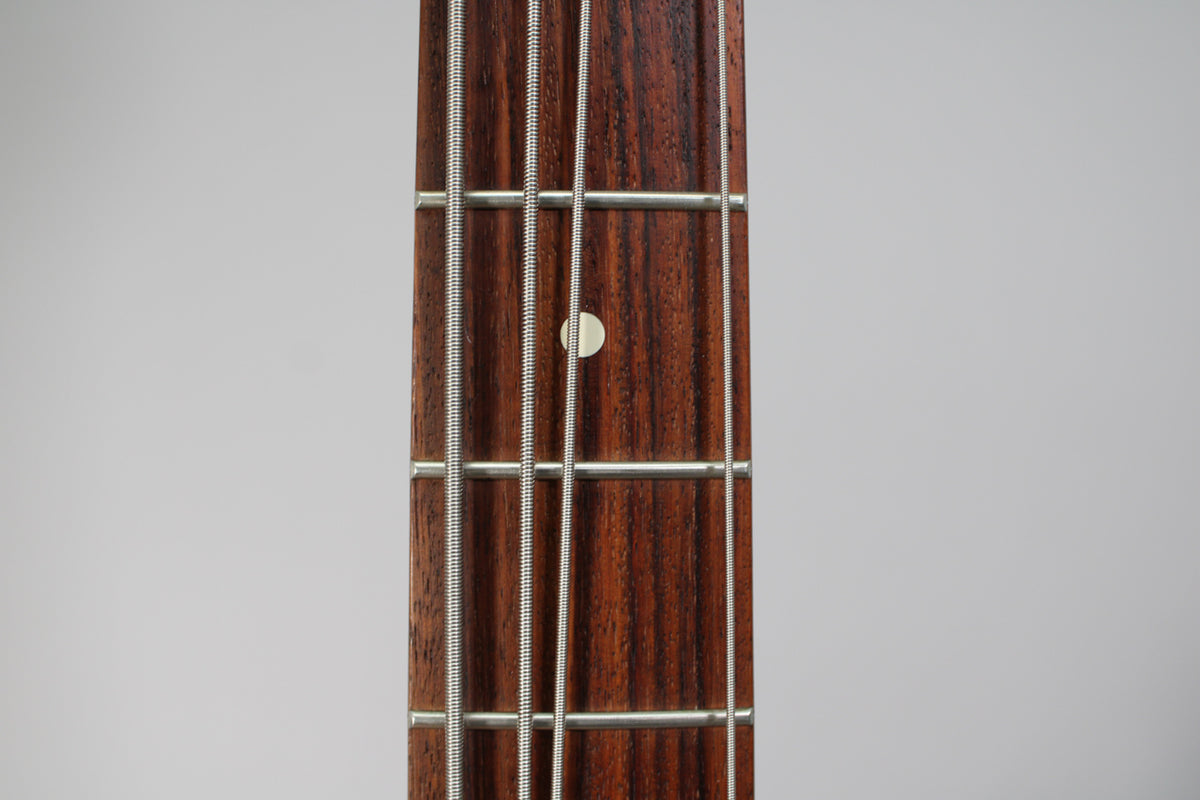 Close-up of the bass's dark rosewood fretboard with four strings, showing a single light-colored fret marker at the 7th fret.