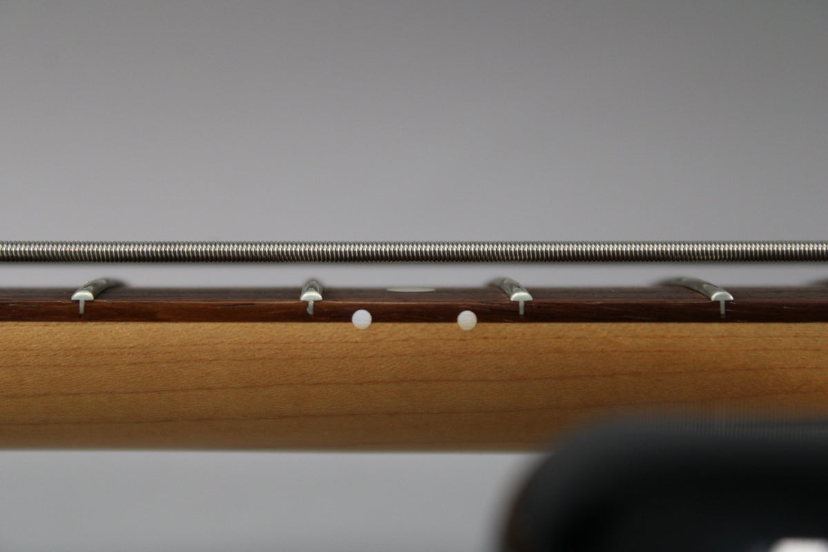 Close-up of the bass neck from the side, showing the maple neck, dark fretboard, frets, and two white side dot markers.