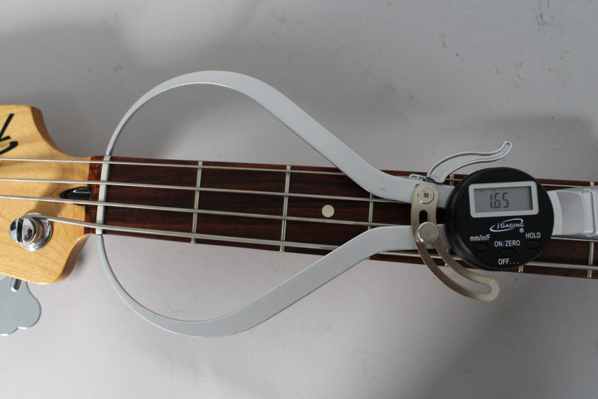 A digital caliper measures the bass guitar's fretboard, displaying "1.65".