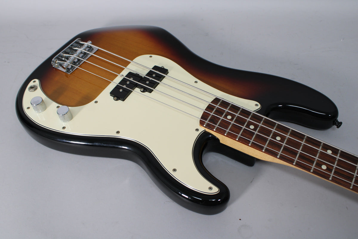 Sunburst bass, angled from above, showing the body, cream pickguard, split pickup, bridge, and part of the fretboard.