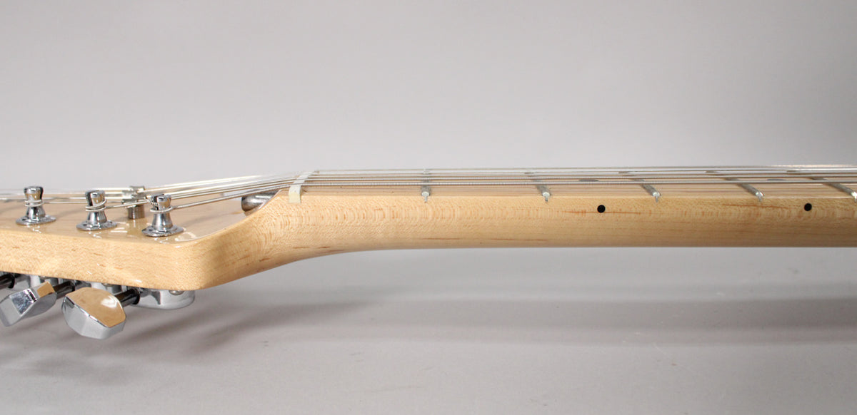 The guitar's light maple neck and headstock are viewed from the side, showing six chrome tuners and a string tree.