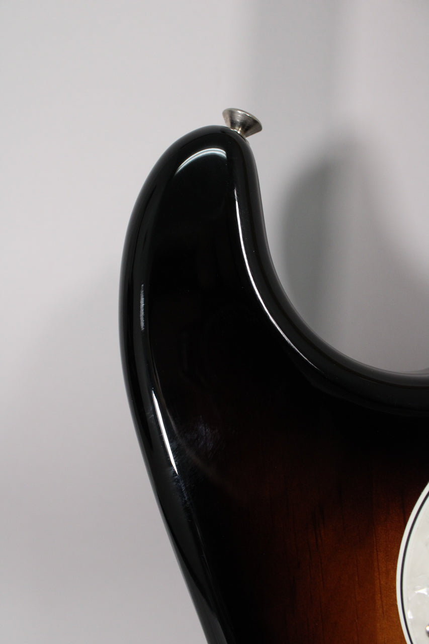 Close-up of the upper horn of a glossy sunburst guitar, showing a chrome strap button and light scratches on the black finish.