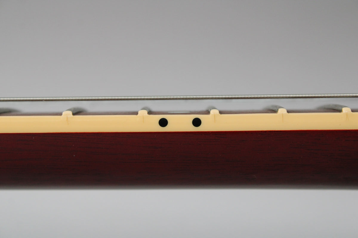 The guitar's dark cherry satin neck is viewed from the side, showing two black dot position markers on the cream binding.