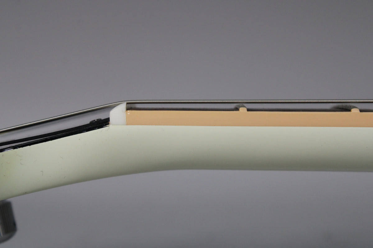 Close-up of the guitar's white neck and headstock transition, showing the nut, strings, and the first few frets of the light brown fretboard.