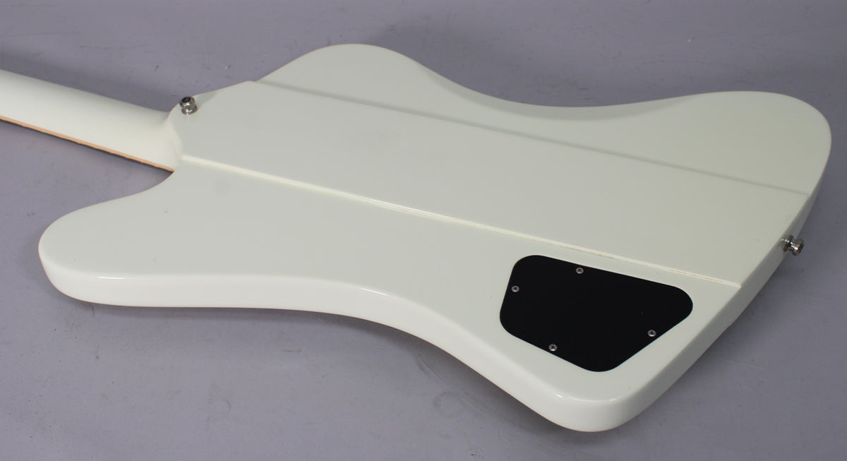 The back of a white Firebird guitar, angled from the neck to the lower bout, showing the control cavity cover and strap buttons.