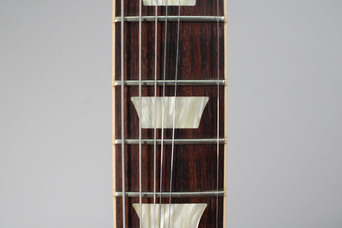 Close-up of the dark rosewood fretboard with trapezoid mother-of-pearl inlays, silver frets, and six strings.