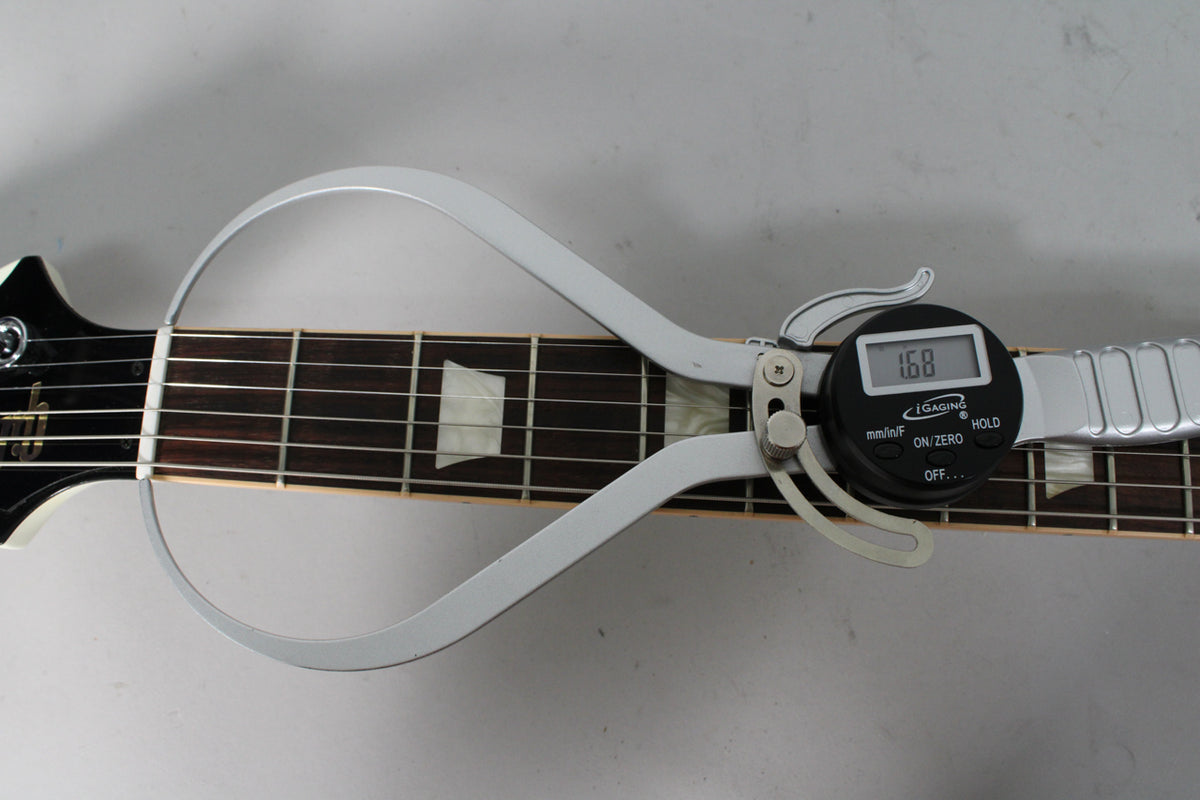 A digital caliper measures the guitar's nut width at 1.68 inches, showing the dark fretboard with trapezoid inlays.