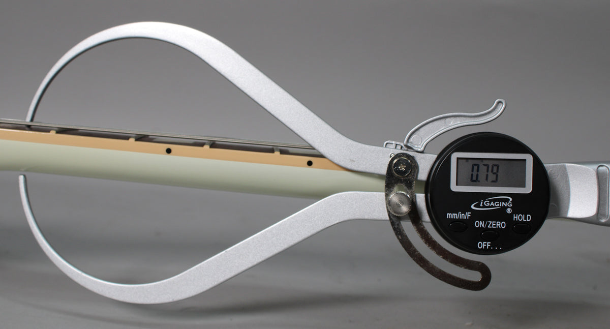 A digital caliper measures the white neck and fretboard, showing a reading of 0.79.