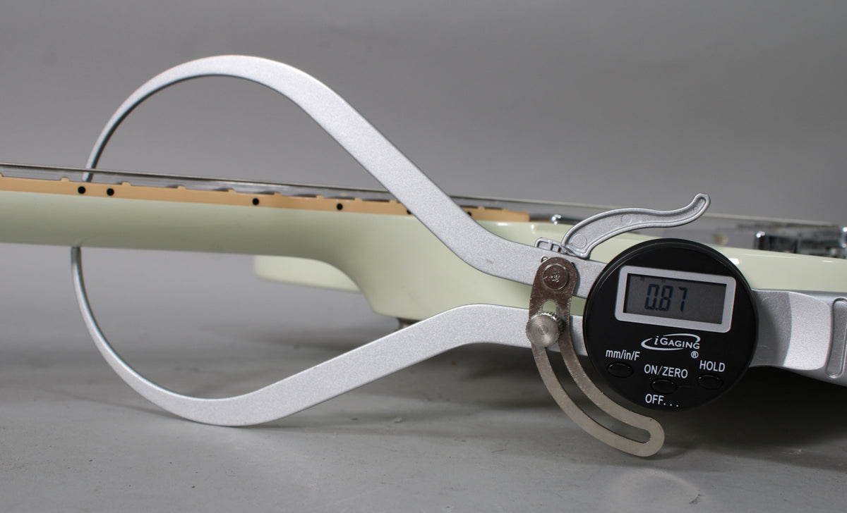 A digital caliper measures the neck relief of the classic white Firebird, showing a reading of 0.87mm on the fretboard.