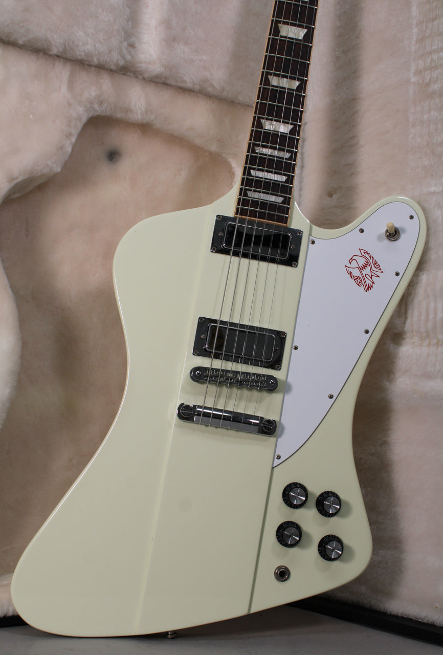 The classic white Firebird body is angled, showing the neck, two humbuckers, tune-o-matic bridge, and four black control knobs.