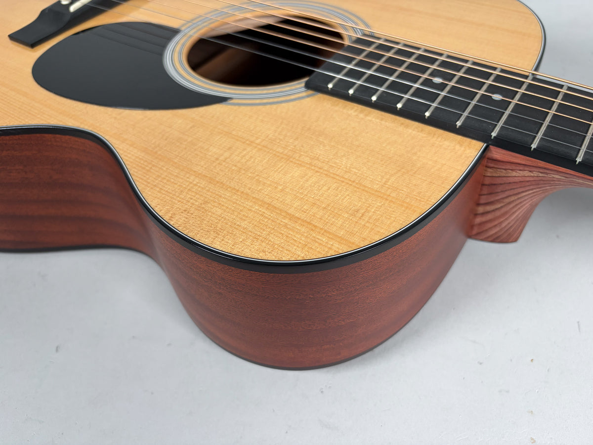 Close-up of the guitar's lower bout, showing the natural wood grain of the light top and darker sides, with a black pickguard.