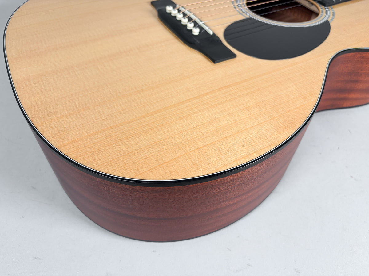 Close-up of the guitar's lower bout, showing the light natural top, dark reddish-brown sides, black pickguard, and bridge pins.
