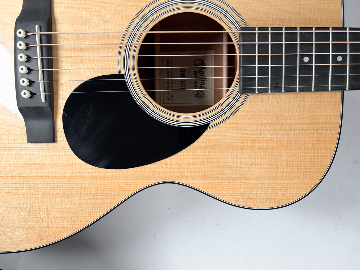 Overhead view of the natural finish acoustic guitar's body, showing the soundhole, black pickguard, bridge, and lower fretboard.