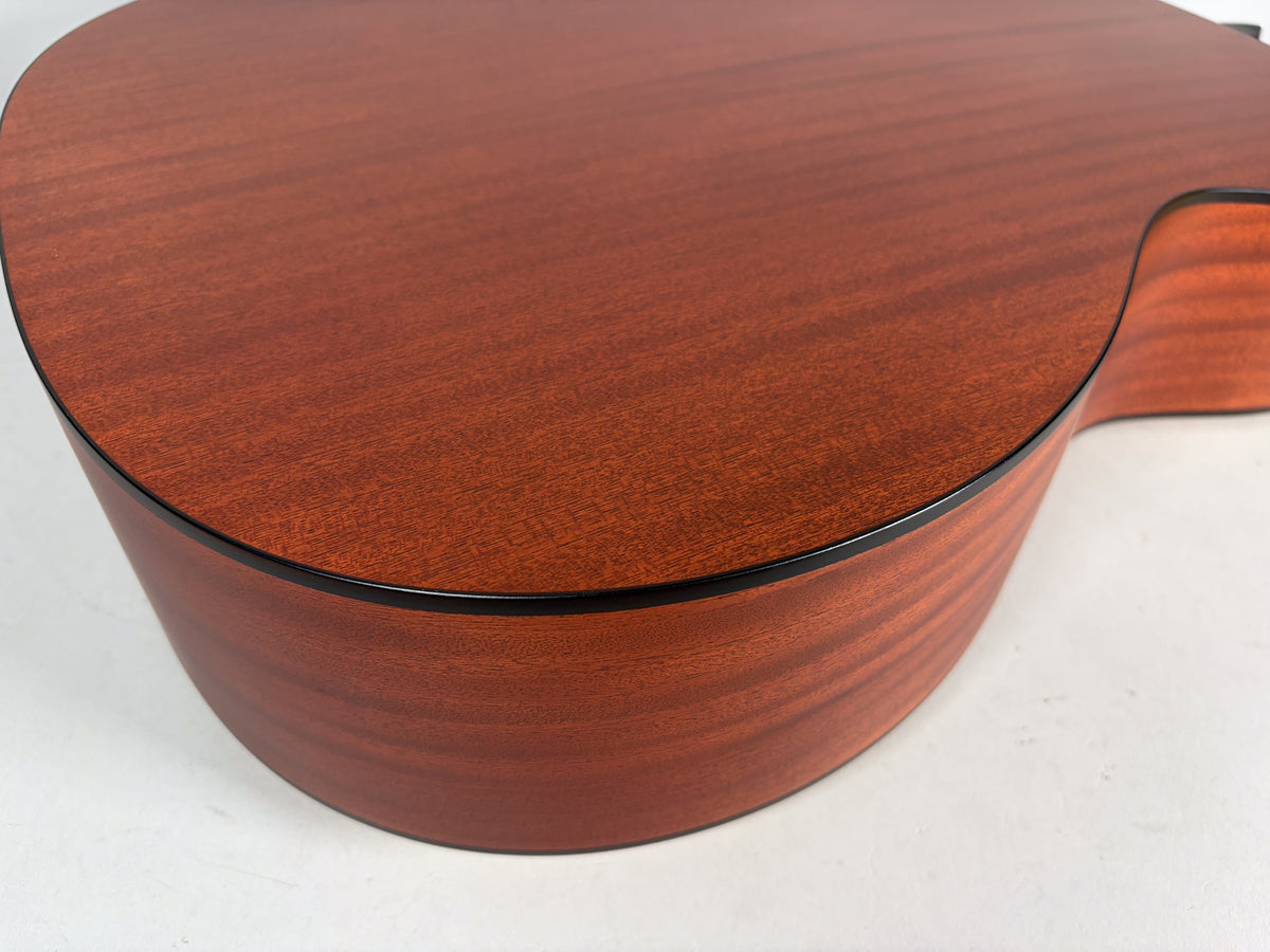 The lower bout and cutaway of the acoustic guitar, showing the reddish-brown wood grain and black binding on the top and side.