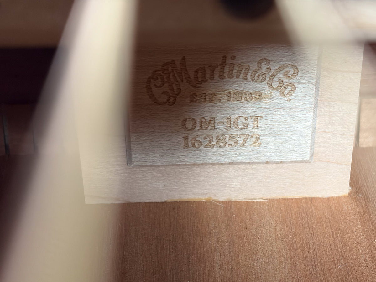 Close-up of the guitar's interior label, showing "Martin & Co." and "OM-1GT" stamped on light wood, with a faint serial number.