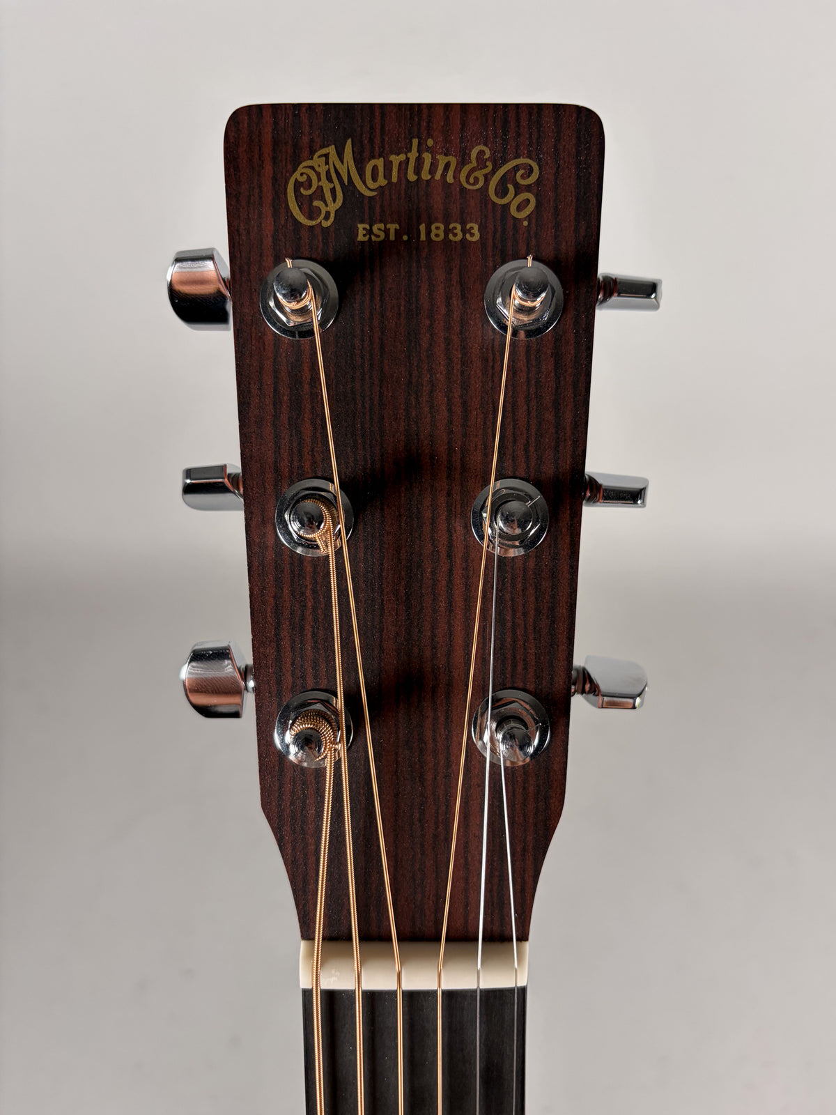 The guitar's dark brown headstock, with a satin finish, is framed from above, showing six chrome tuners and a cream nut.