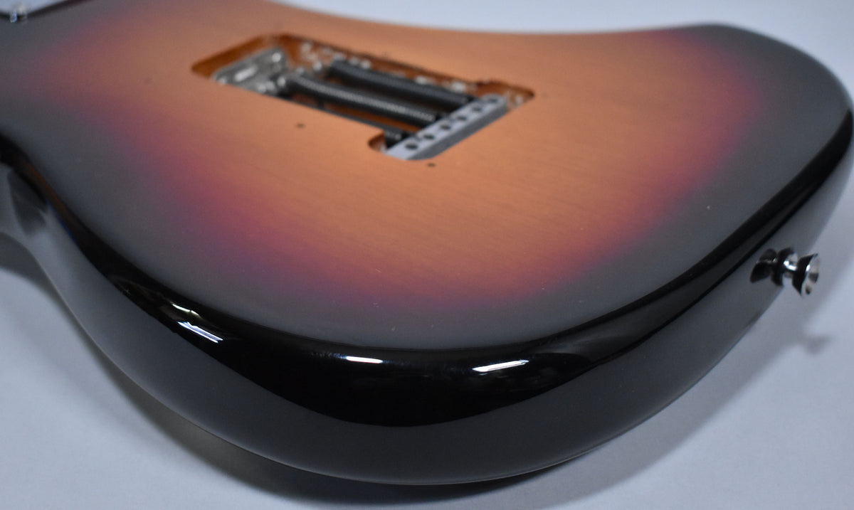 The guitar's sunburst body, with a visible tremolo spring cavity and output jack, shows minor scuffs on its glossy black edge.