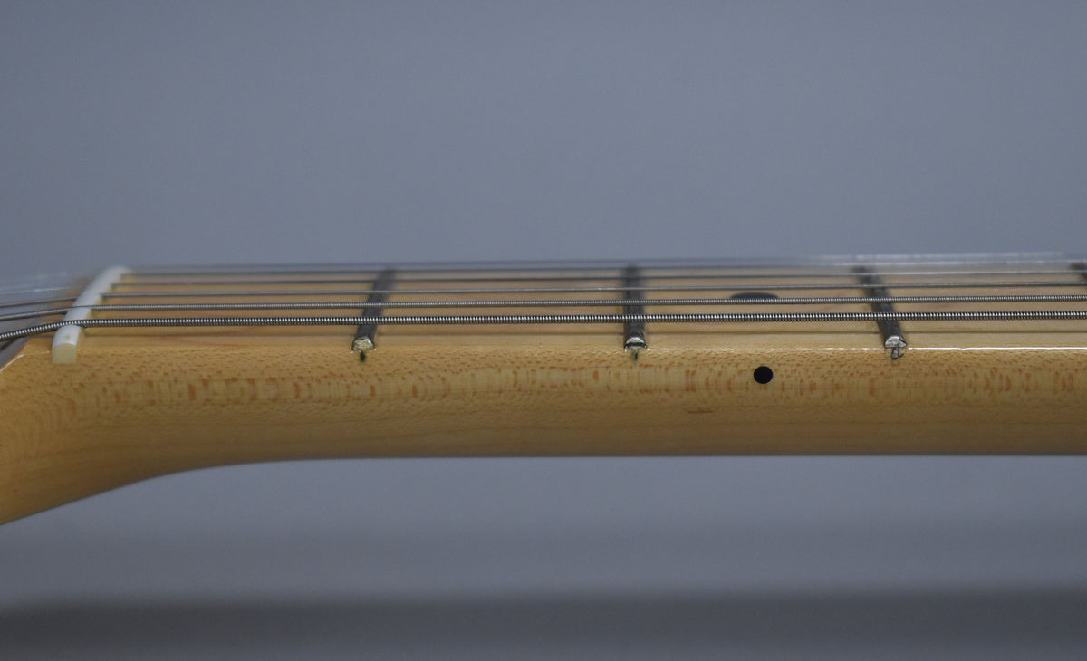 Close-up of the light maple neck and fretboard from the side, showing the nut, frets, strings, and a black dot inlay.