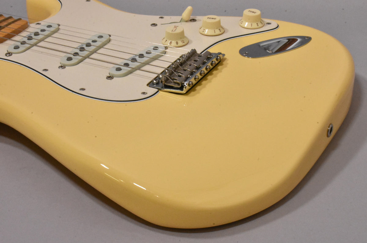Upper body of a vintage white Stratocaster, showing three single-coil pickups, chrome tremolo bridge, and three cream control knobs.