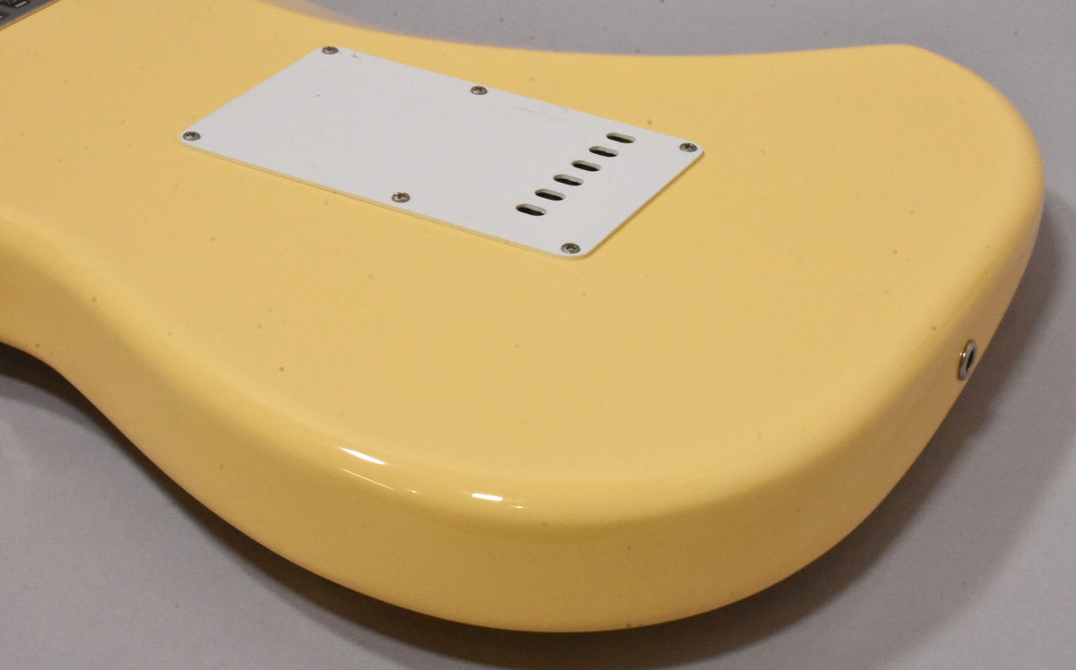 The back of a vintage white Stratocaster body, showing the tremolo cavity cover, output jack, and light finish wear.