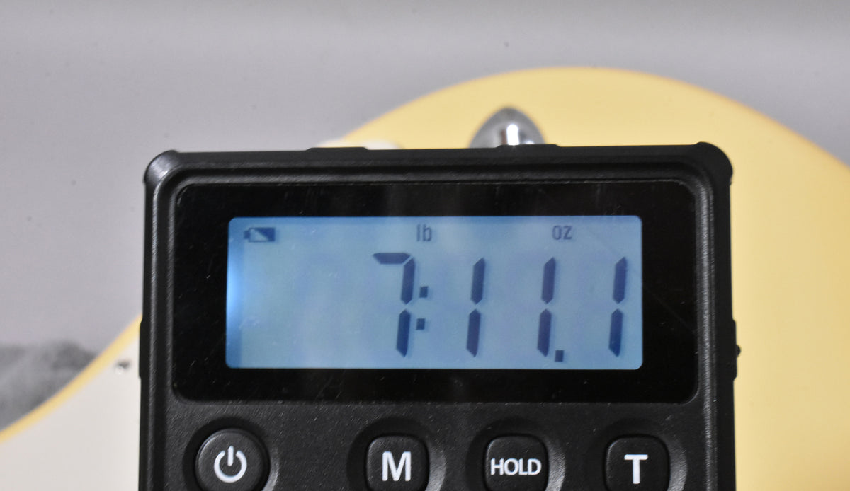 A digital scale displays "7 lb 1.1 oz" with the vintage white guitar body visible in the background.