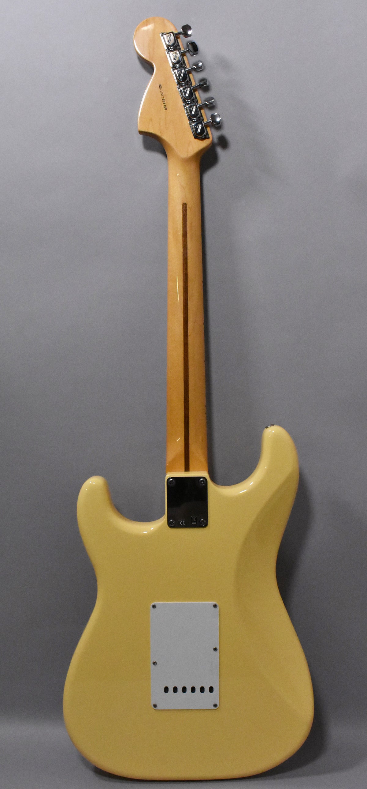 The back of a vintage white Stratocaster, showing the light maple neck, chrome tuners, black neck plate, and tremolo cavity cover.