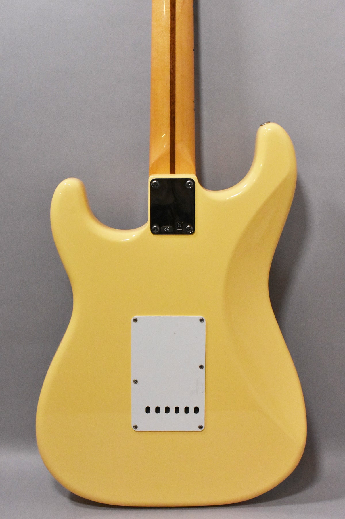 The back of a vintage white Stratocaster, showing the neck joint, light-colored maple neck, and white tremolo cover.