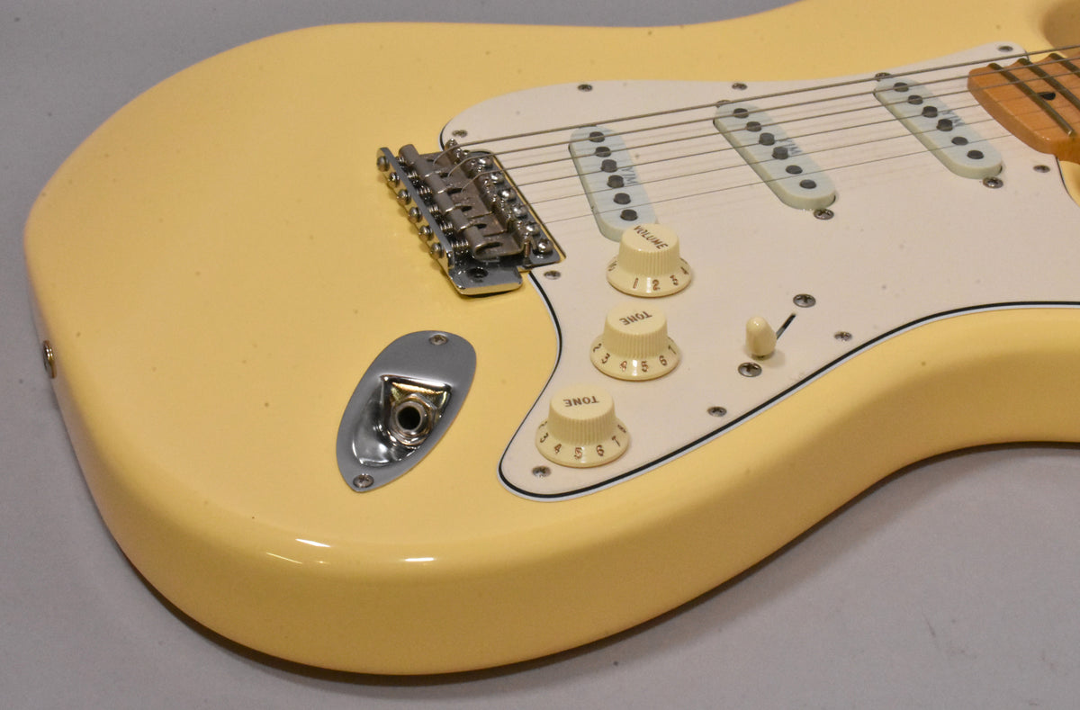 Close-up of the vintage white Stratocaster body, showing the input jack, tremolo bridge, white pickguard, and three cream control knobs.