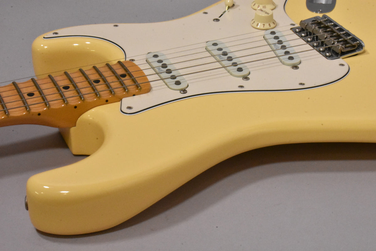 Upper body of a vintage white Stratocaster, showing the maple fretboard, white pickguard, three single-coil pickups, and chrome tremolo.