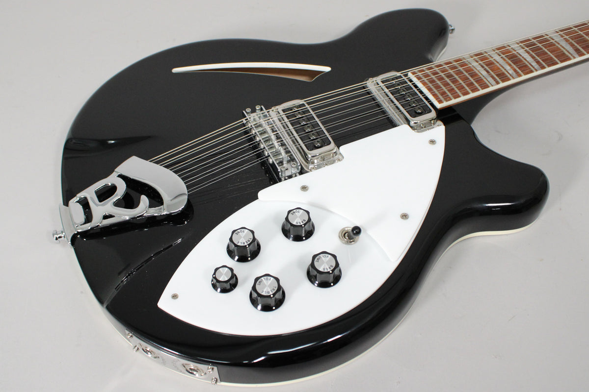 The black 12-string electric guitar is angled from the lower left, showing its white pickguard, five control knobs, and chrome hardware.