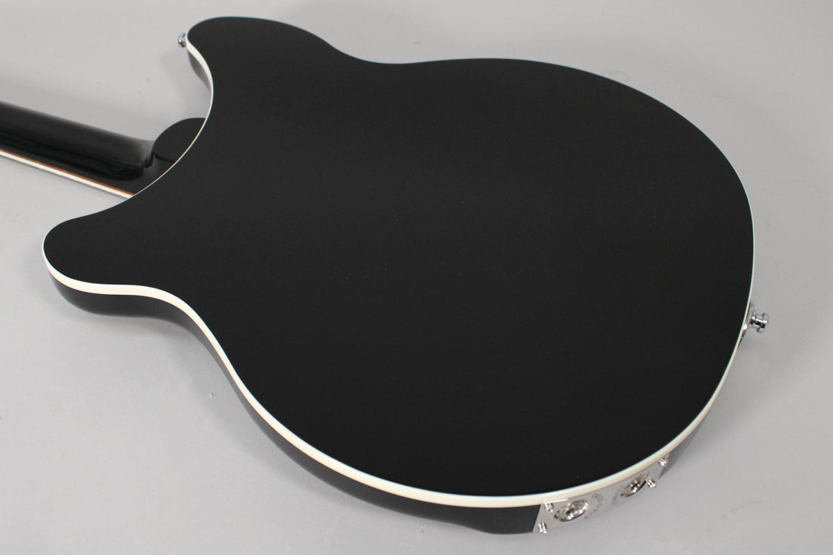 The guitar's glossy black back, with white binding, is angled from the neck joint to the chrome output jacks.