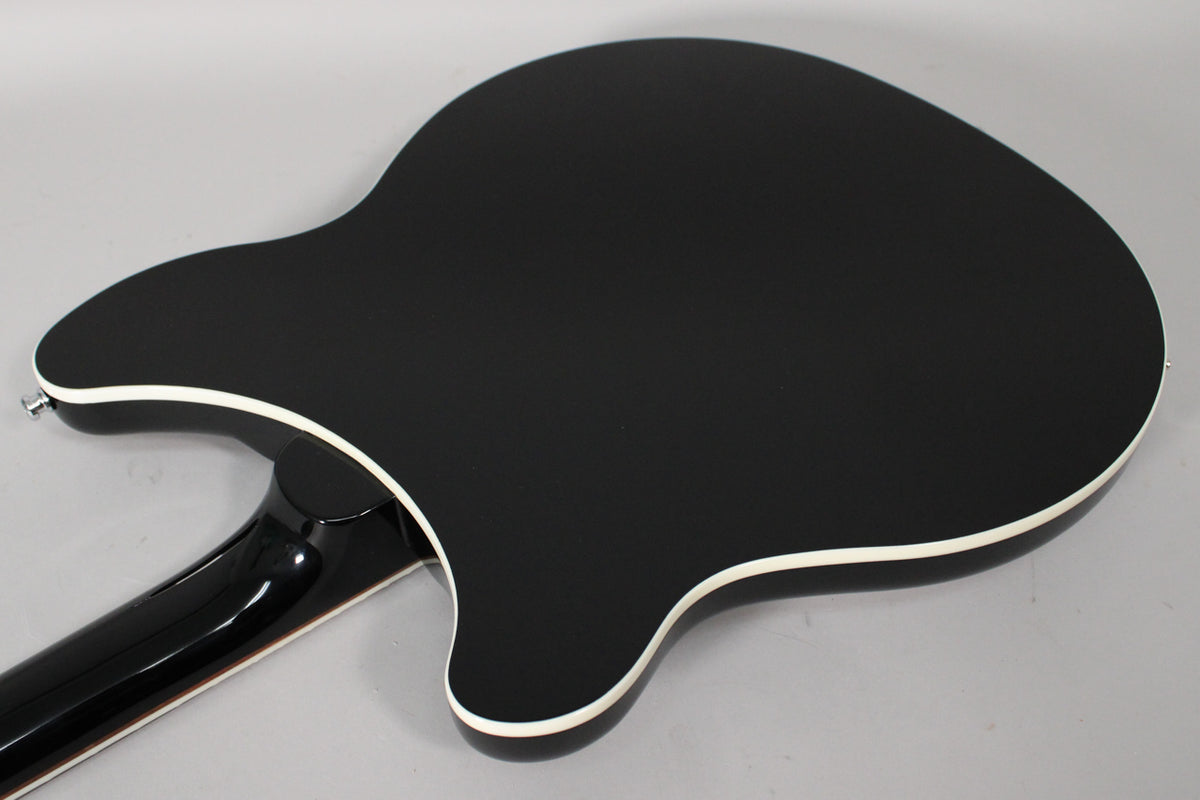 The back of a black guitar with white binding, showing the neck joint and a chrome strap button.