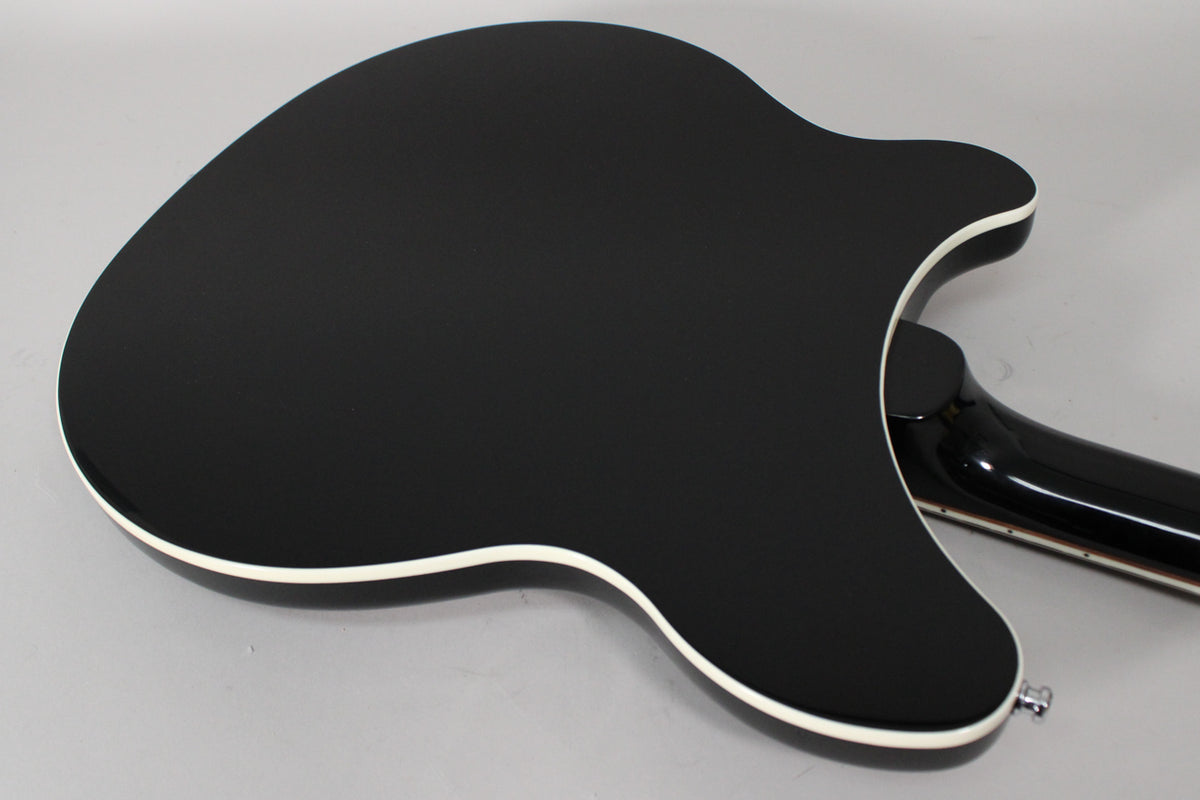 The back of the glossy black guitar is shown from an angle, revealing its white binding and the neck joint.
