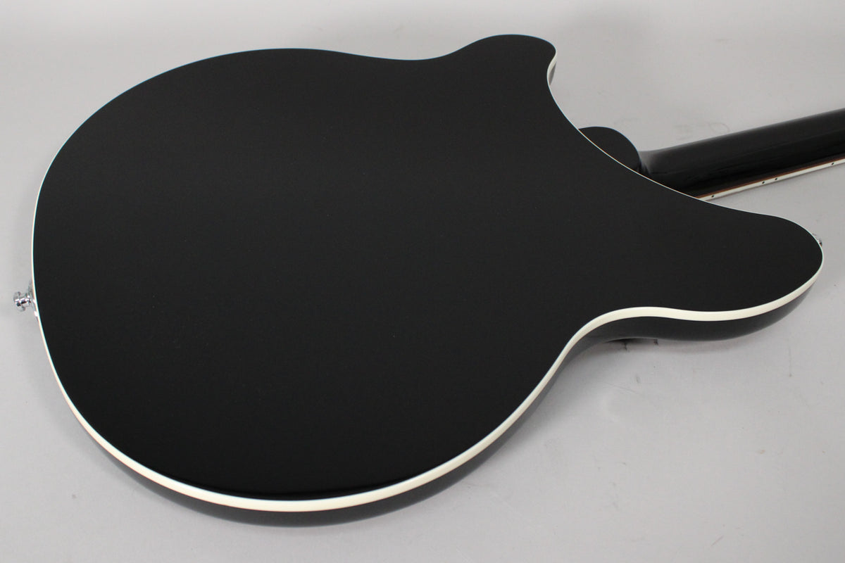 The back of a black electric guitar with white binding, angled from the lower left, showing the neck joint and strap button.