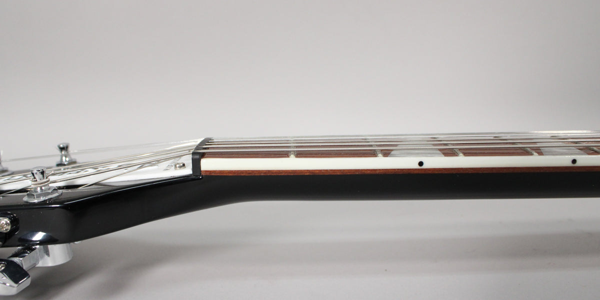 Close-up of the guitar's glossy black headstock and neck, showing the nut, fretboard with white binding, and chrome tuners.