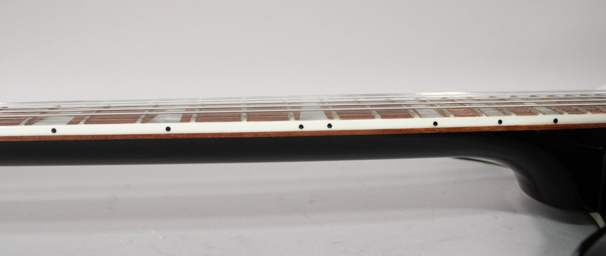 Close-up of the guitar's black neck and dark brown fretboard with white binding and small black dot inlays.