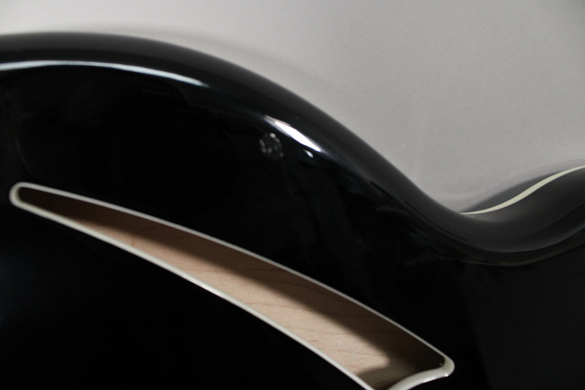 Close-up of the guitar's upper bout, showing a small ding on the glossy black finish above the f-hole with cream binding.