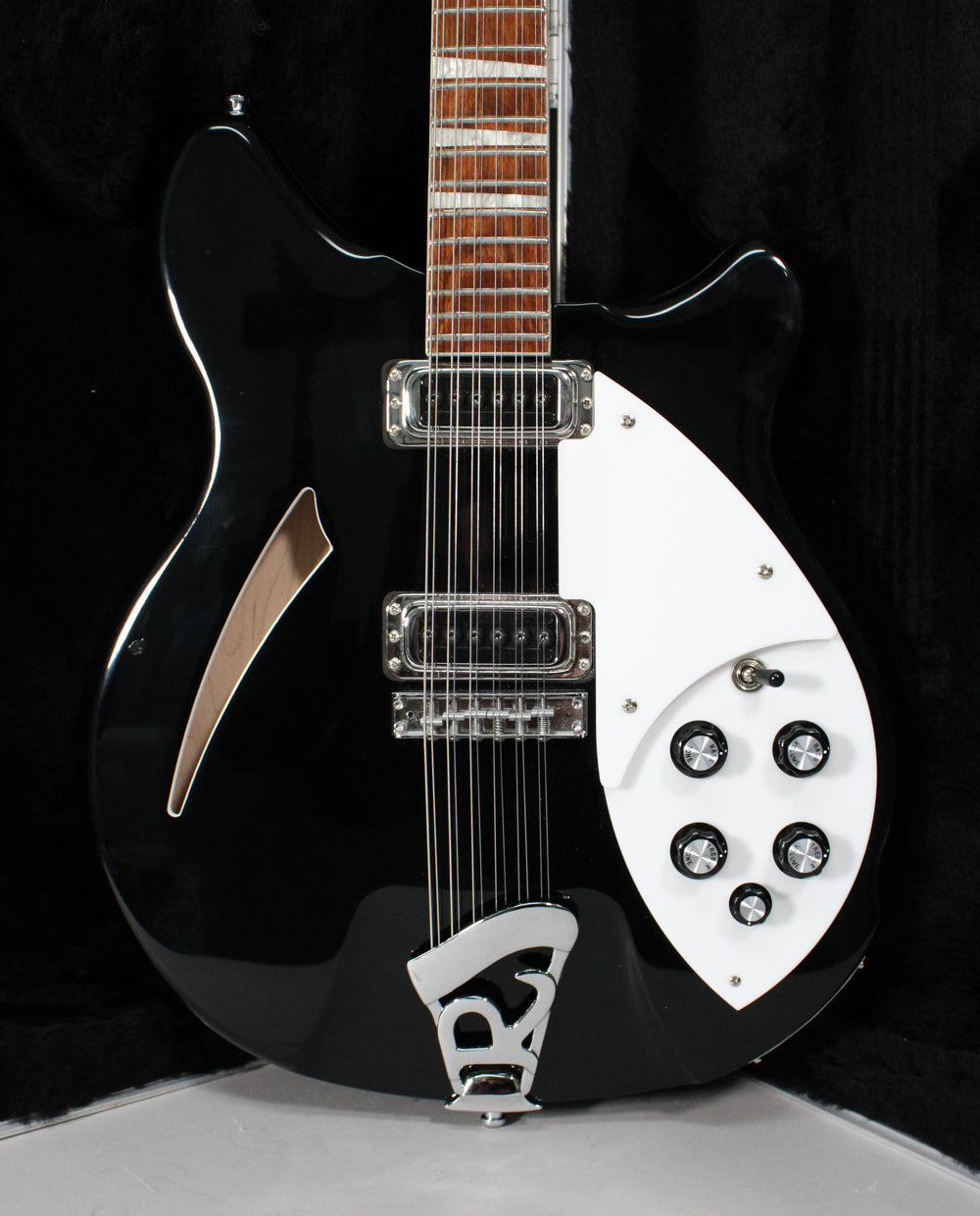 Full-frame view of a glossy black 12-string electric guitar with a white pickguard, chrome hardware, and a light wood f-hole.
