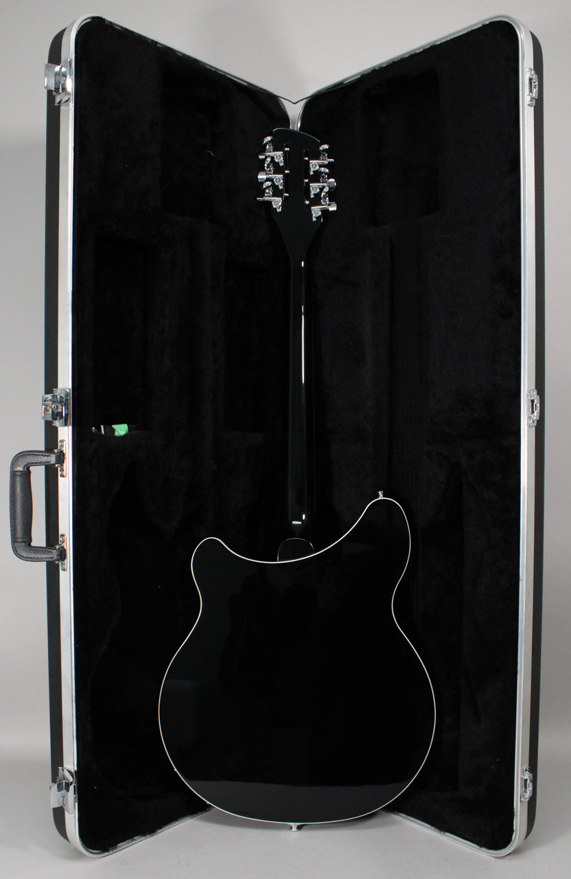 The black guitar, with a glossy finish and white binding, is seen from the back in its open, black-lined hard case.