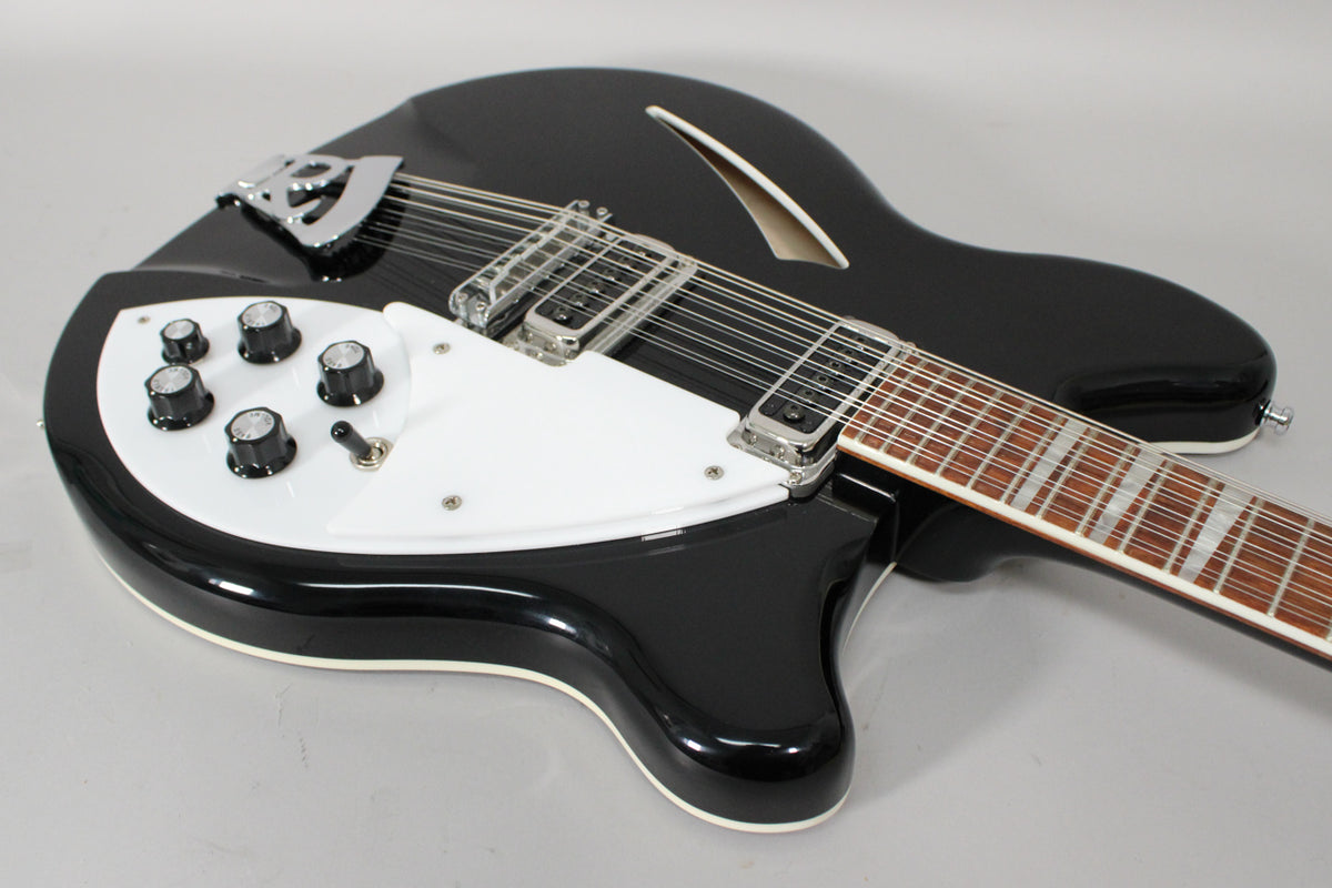 Black 12-string electric guitar, angled from above, showing the body, white pickguard, chrome hardware, and f-hole.