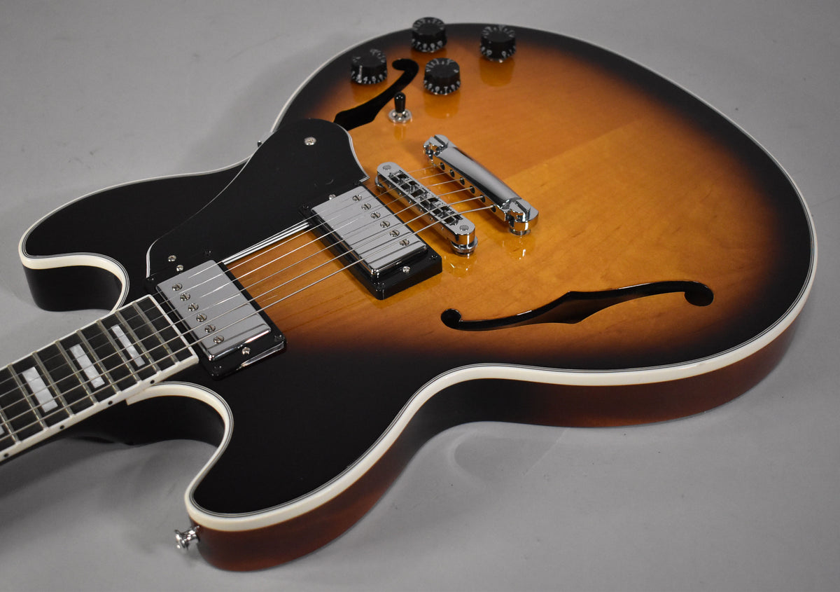 A sunburst semi-hollow guitar, angled from the lower bout, showing its black pickguard, chrome hardware, and f-holes.