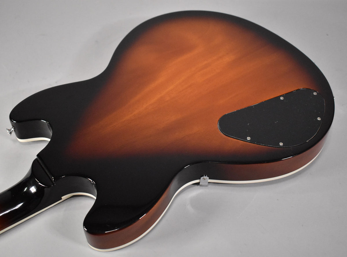 The guitar's back, in vintage sunburst with a glossy finish and cream binding, shows a black control cavity cover.