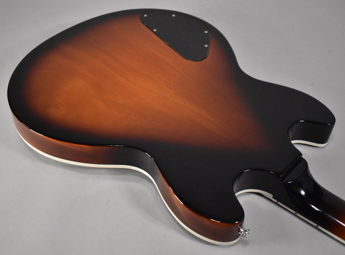 The guitar's back, in vintage sunburst, shows a black control cavity cover and a chrome strap button on the lower bout.