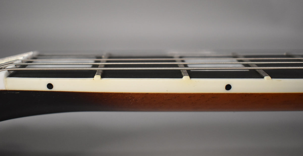 Close-up of the guitar's fretboard binding, showing cream-colored binding with dark side dots and a dark brown neck finish.