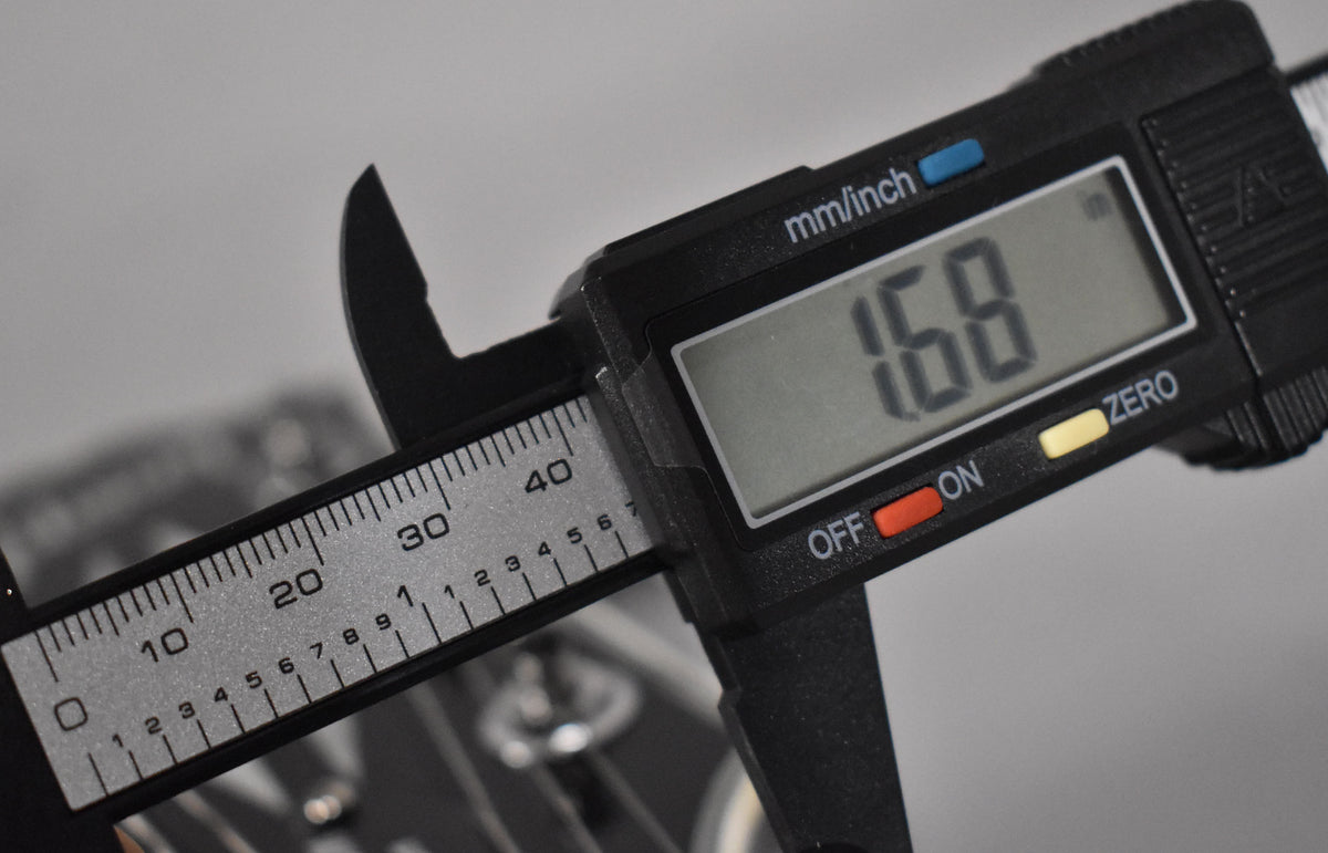 A digital caliper measures the nut width at 1.68 inches, with the guitar's headstock and tuners blurred in the background.